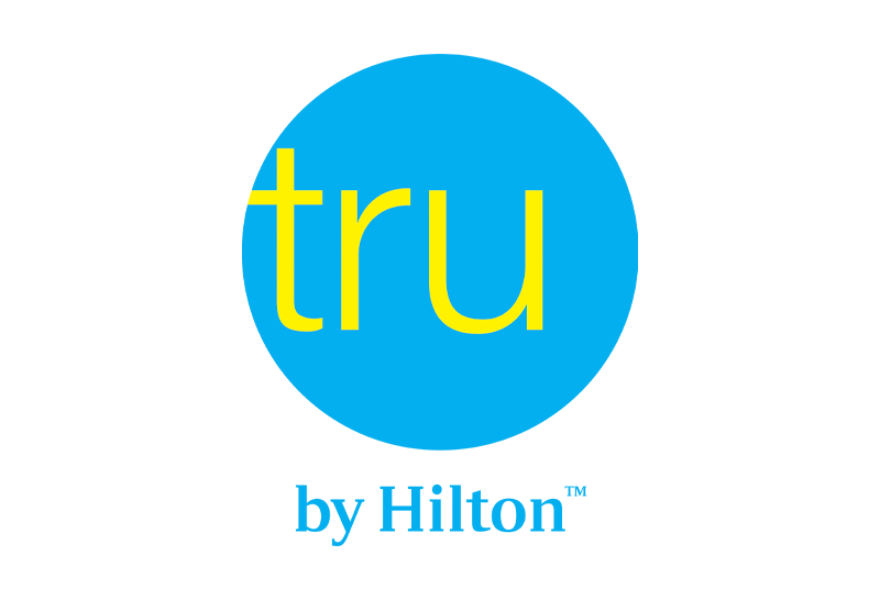 Logotipo de Tru by Hilton con texto amarillo dentro de un círculo azul claro.